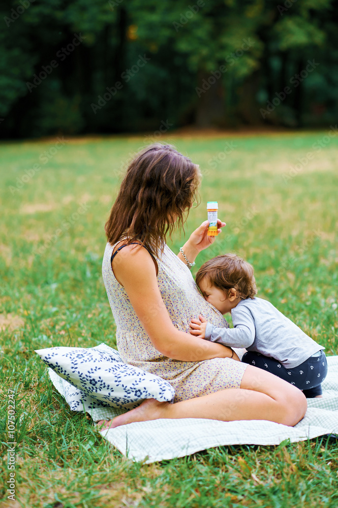 Young pregnant mother resting with her son in summer park and bl Young pregnant mother resting with her son in summer park and bl