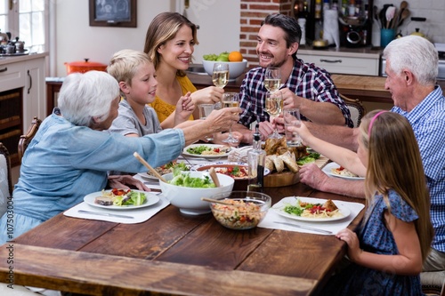 Multi-generation family toasting glass of wine while having meal