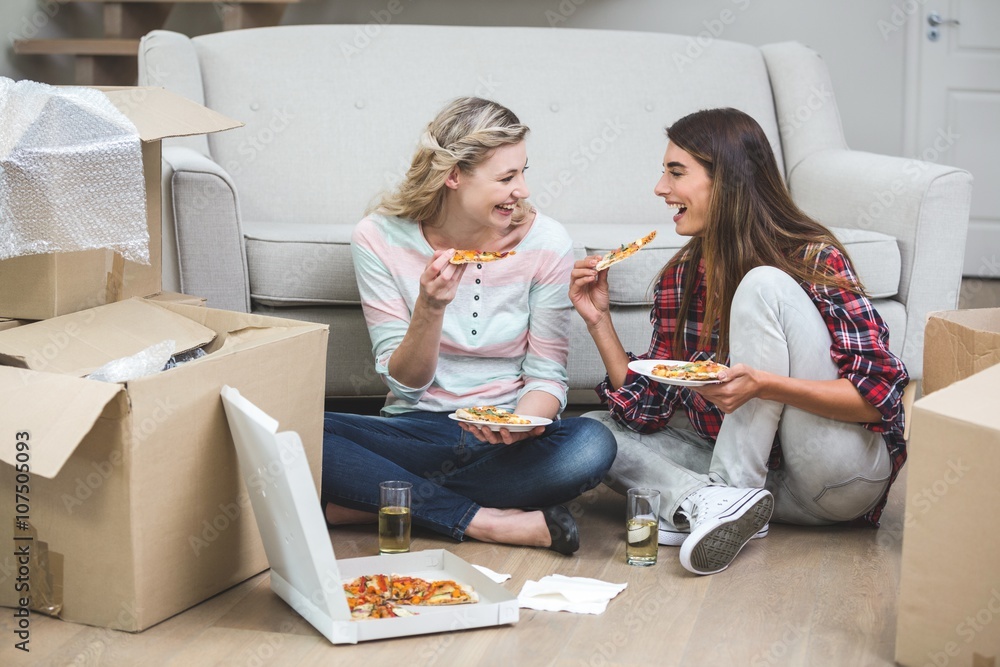 Fototapeta premium Two beautiful woman having pizza in the new house