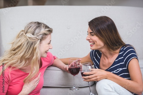 Two beautiful women holding glass of wine and talking in the living room at home