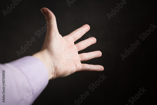Hand of a man reaching to somewhere on dark background.