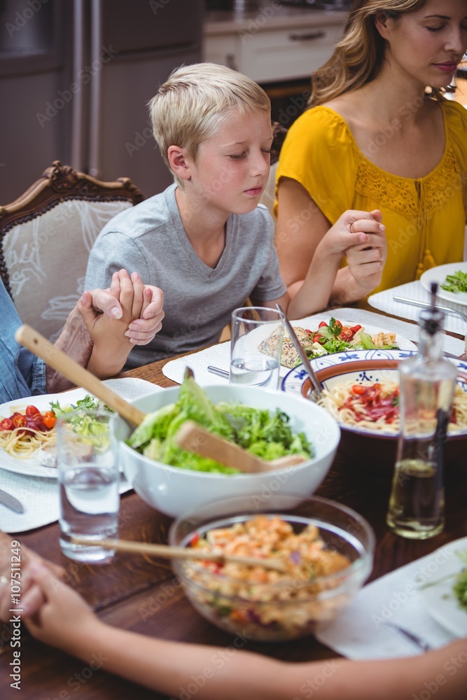 Family holding hands while praying at dining table