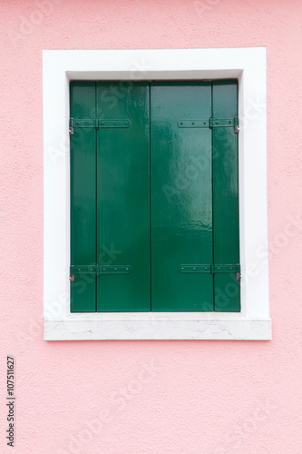 Old window with dark green shutters on light pink wall