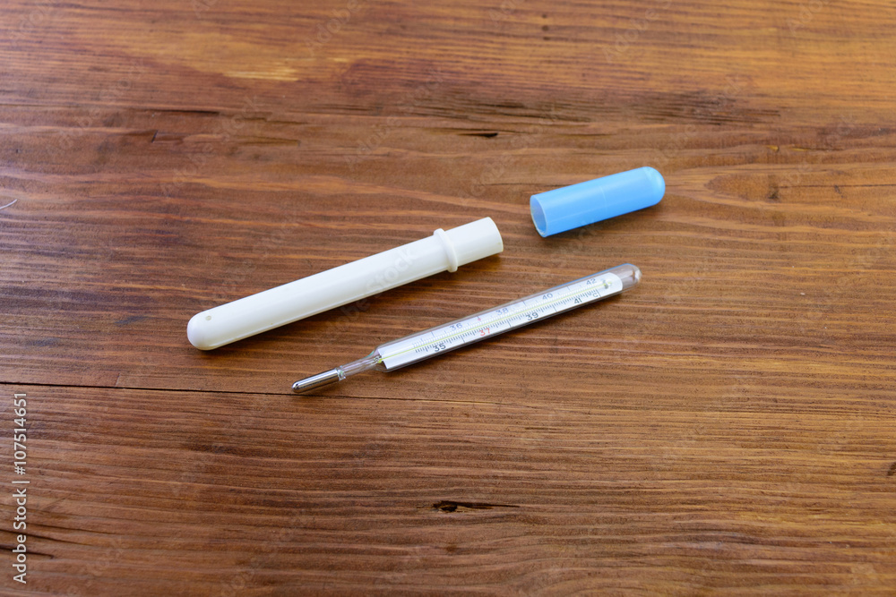 macro glass mercury thermometer with a plastic protective cover on a wooden background macro glass mercury thermometer with a plastic protective cover on a wooden background