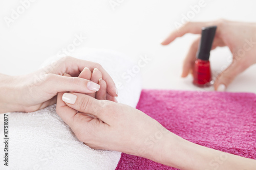 Woman applying red nail varnish to finger nails. Woman is having