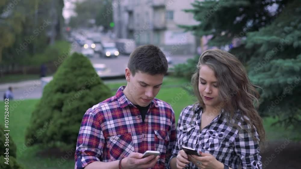 Young happy couple using smart phones near a trees in a center Young happy couple using smart phones near a trees in a center