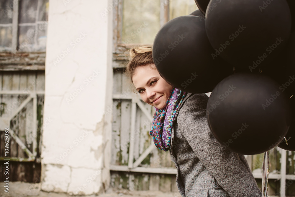 Pretty young woman with black balloons in vintage street background 