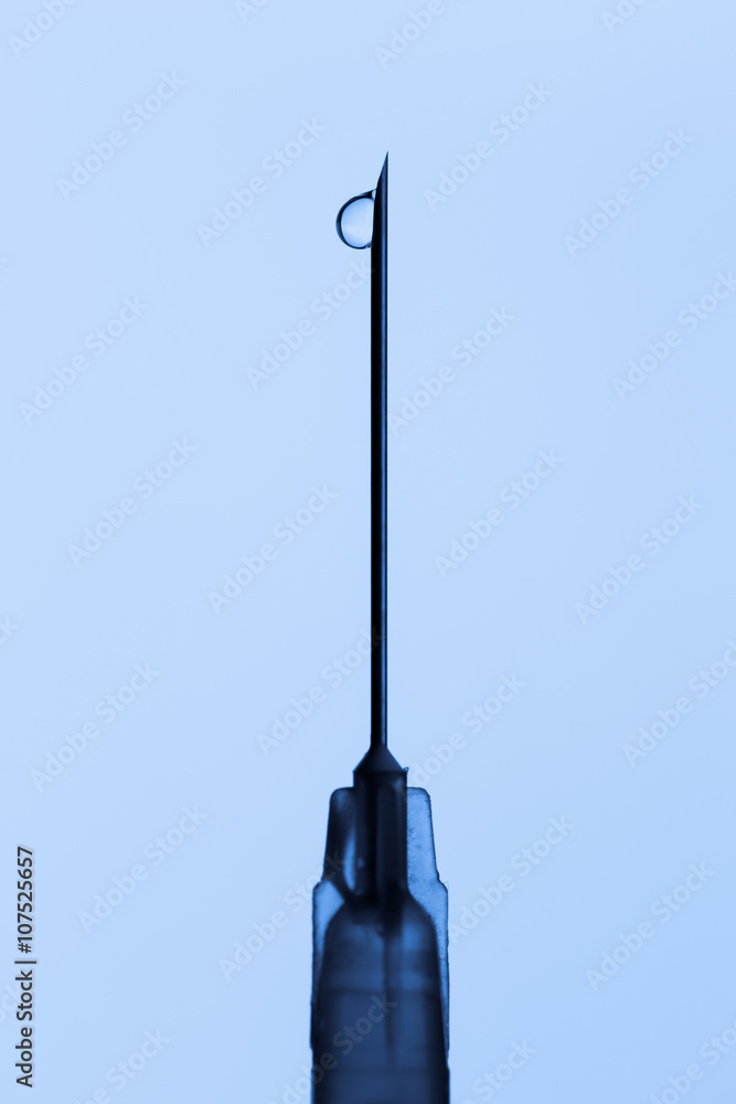 tip of medical syringe needle with drop of medicine in blue color tone. tip of medical syringe needle with drop of medicine in blue color tone.