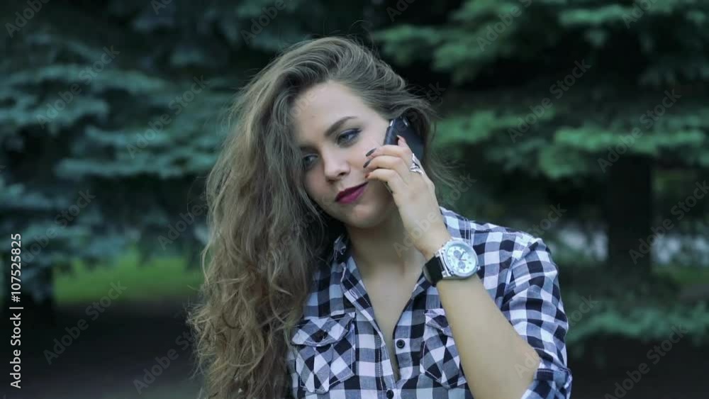 Young girl touching her hair and speaking on a phone by nature background Young girl touching her hair and speaking on a phone by nature background