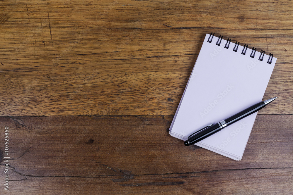 White sheets notebook with spiral on right side of the wooden dark brown table with black pen on it from above White sheets notebook with spiral on right side of the wooden dark brown table with black pen on it from above