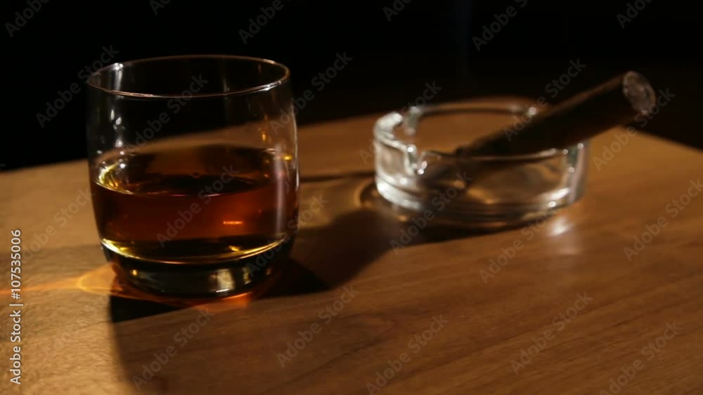 Glass of whiskey with smoking cigar.Glass of alcohol and smoking noble cigar on a black background.Rotating glasses of whiskey with smoking cigar. Glass of whiskey with smoking cigar.Glass of alcohol and smoking noble cigar on a black background.Rotating glasses of whiskey with smoking cigar.