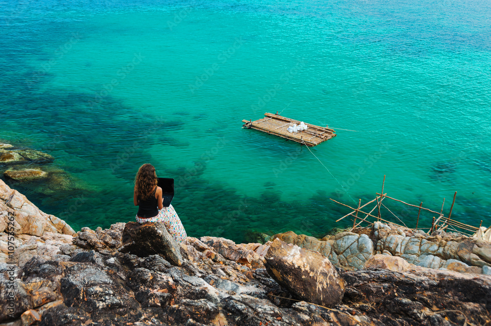 Woman freelancer feeling happy with laptop. Amazing seaview with blue lagoon with rocks.