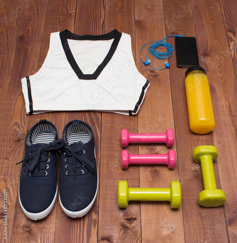 Sport accessories: clothes, shoes, weights, bottle, phone on wooden background