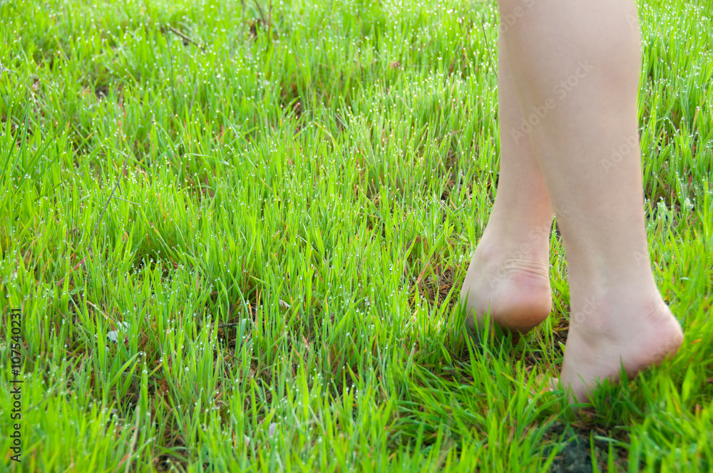 Close-up of female legs walking on green grass barefoot