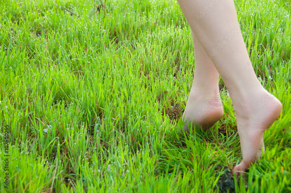 Close-up of female legs walking on green grass barefoot