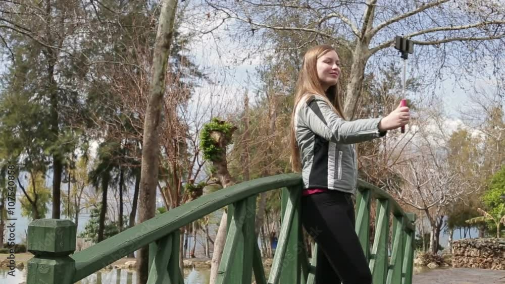 Young happy woman taking self portrait standing on the wooden bridge using smartphone mobile cell phone camera. Closeup. HD 1920x1080. Young happy woman taking self portrait standing on the wooden bridge using smartphone mobile cell phone camera. Closeup. HD 1920x1080.