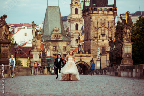 Happy handsome groom chasing after beautiful bride on Prague bri