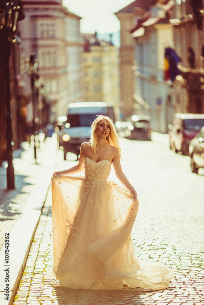 Naklejka premium Beautiful fairytale blonde bride posing in empty street at sunri