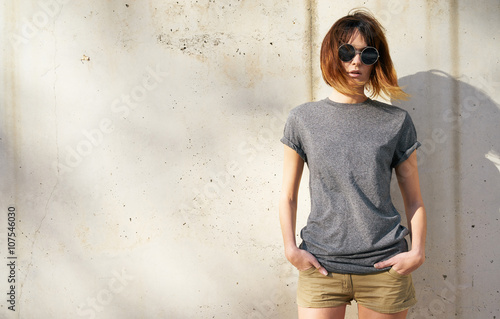 attractive young woman dressed in a gray blank t-shirt posing on a background of a concrete wall in the rays of the setting sun