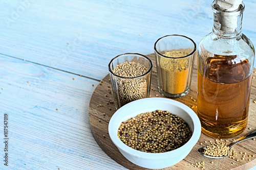 
Mustard.  Mustard seeds, mustard powder, mustard oil in glassware and mustard in a white  cup on a wooden board

 