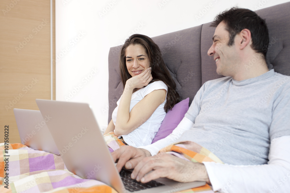 Young man and woman working in bed, focus on woman Young man and woman working in bed, focus on woman