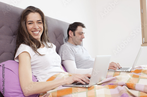 Young man and woman working in bed, focus on woman