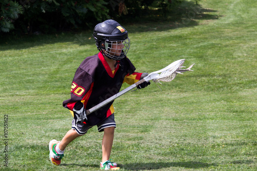 Child wearing black jersey and protective equipment playing lacr