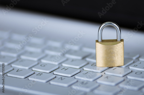 Small padlock sitting on white computer keyboard, online security concept