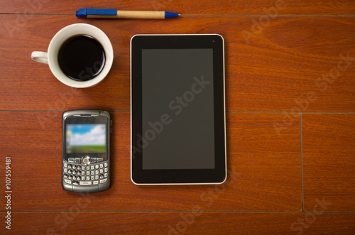 Notepad, mobile phone, tablet and coffee cup as seen from above sitting on wooden surface