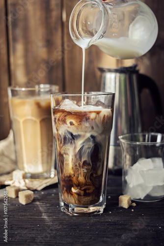Iced coffee in two glasses with poured milk 