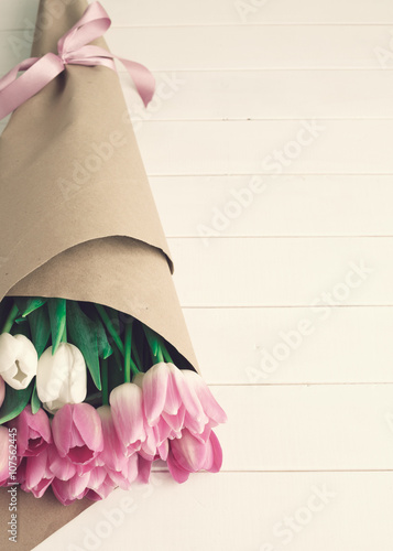 Fototapeta Naklejka Na Ścianę i Meble -  Pink and white tulips wrapped in brown paper over white wood