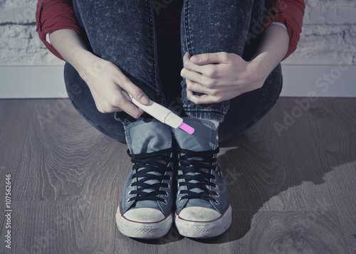 pregnant teenager girl or young desperate woman holding positive pink pregnancy test