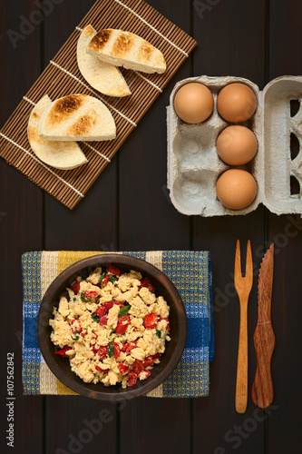 Scrambled eggs made with red bell pepper and green onion in rustic bowl with toasted bread and eggs, photographed on dark wood with natural light