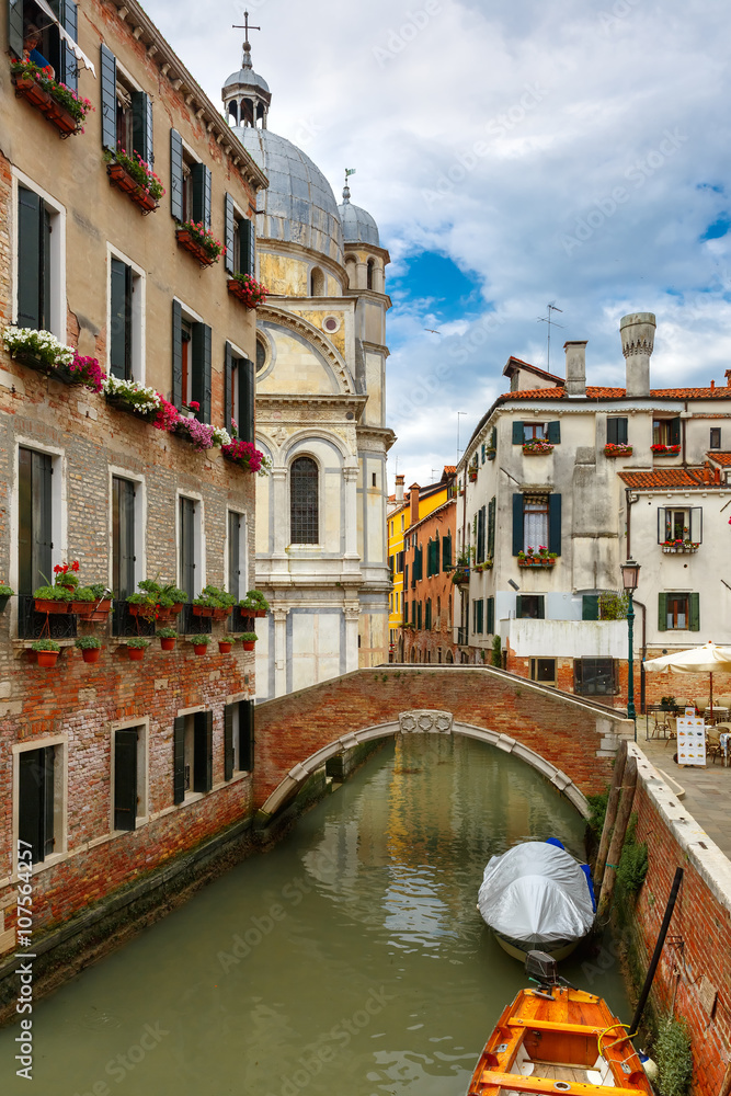 Colorful narrow lateral canal, church Santa Maria dei Miracoli and pedestrian bridge in the sestiere of Cannaregio at morning, in Venice, Italia