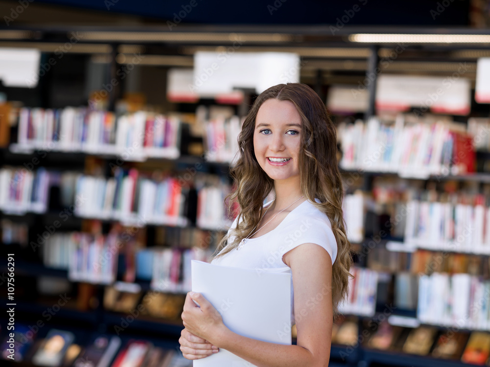 Happy female student holding books at the library Happy female student holding books at the library