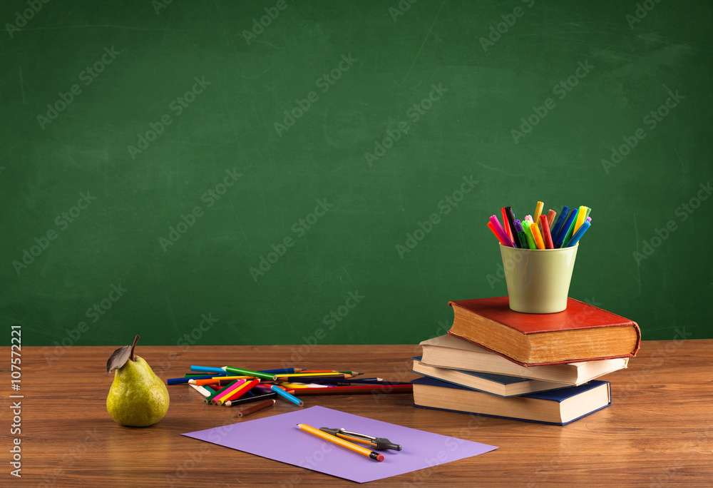 School items on desk with empty chalkboard School items on desk with empty chalkboard