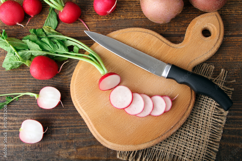 red potatoes on wooden brown background near a cutting Board with sliced radishes on wooden brown background red potatoes on wooden brown background near a cutting Board with sliced radishes on wooden brown background