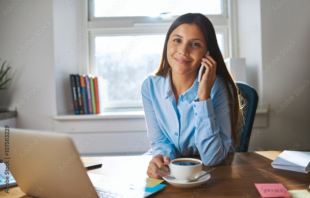 Smiling female on phone with coffee and computer Smiling female on phone with coffee and computer