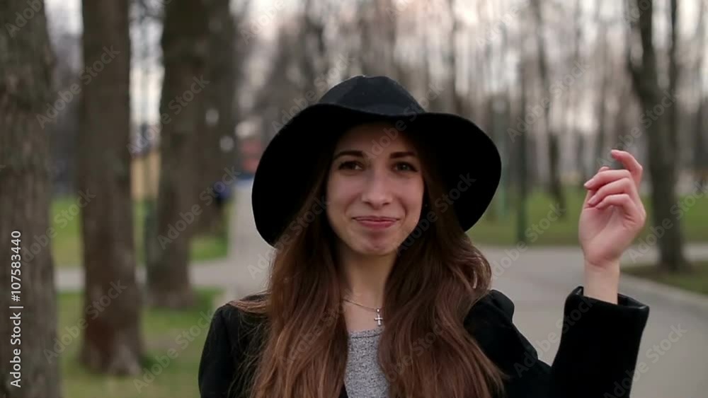Young pretty girl with a black hat smiles happily into camera, close up, slow motion