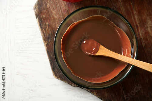 Melted chocolate in glass bowl, on wooden background