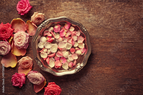 Pink and white rose petals in silver bowl with water on wooden background
