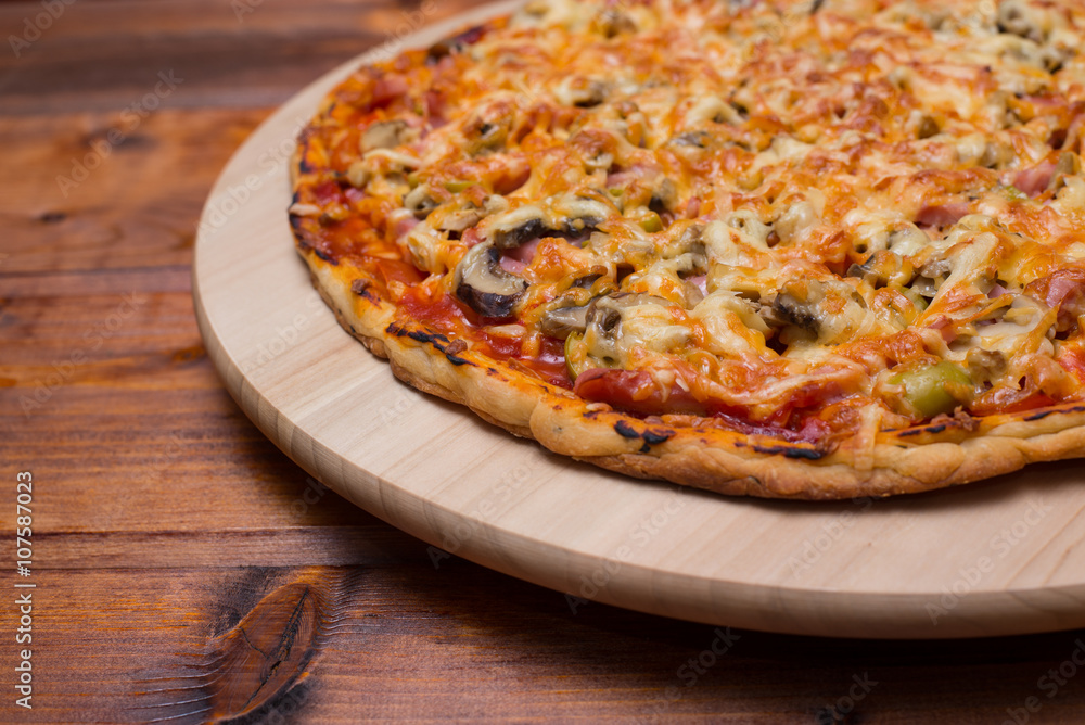 Italian pizza with ham and mushrooms on a wooden board on natural wooden table