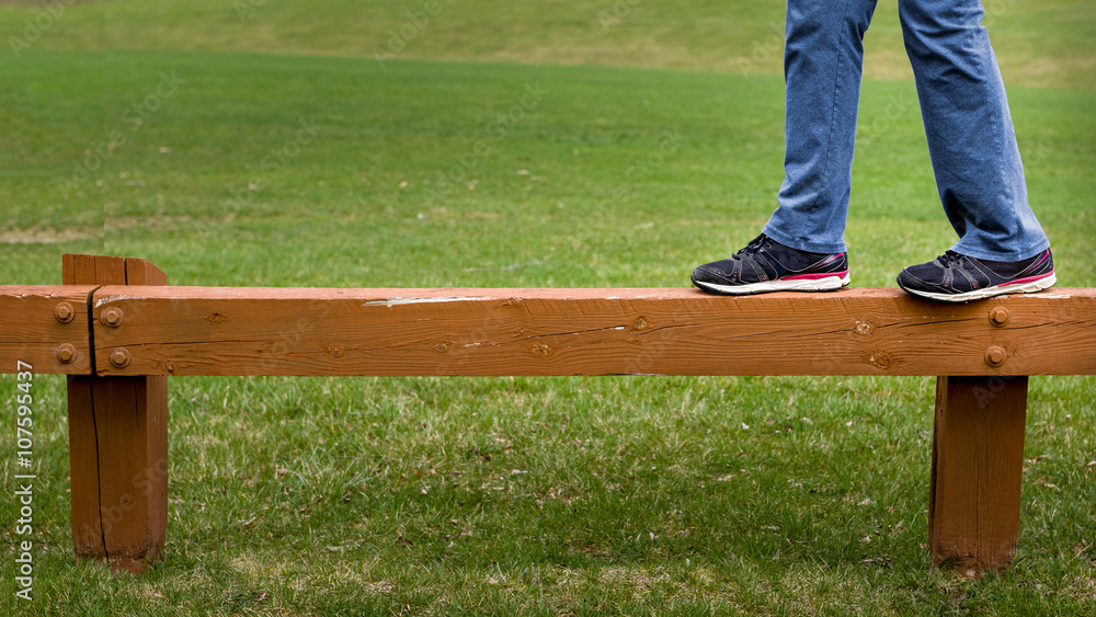 Closeup of person walking on wooden guard rail in park