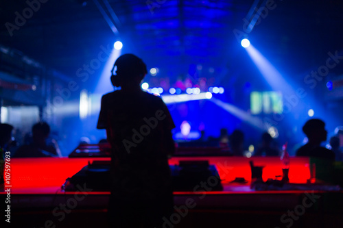 Blurred background : Club, disco DJ playing and mixing music for crowd of happy people. Nightlife, concert lights, flares