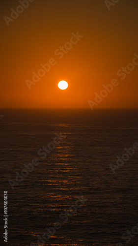 scenic sunset over the sea, sun turns red few moments before disappearing behind the water horizon © marinzolich