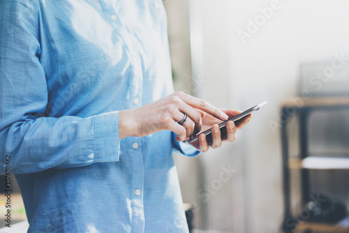Photo business woman wearing jeans shirt, touching smartphone screen. Modern loft office. Blurred background, sunlight. Horizontal mockup. Film effect