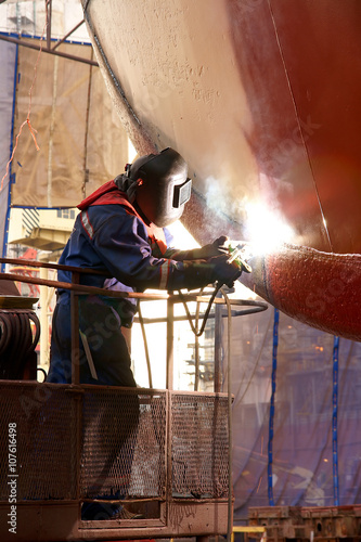 Shipyard welder welding the hull of the ship at the dock with lift