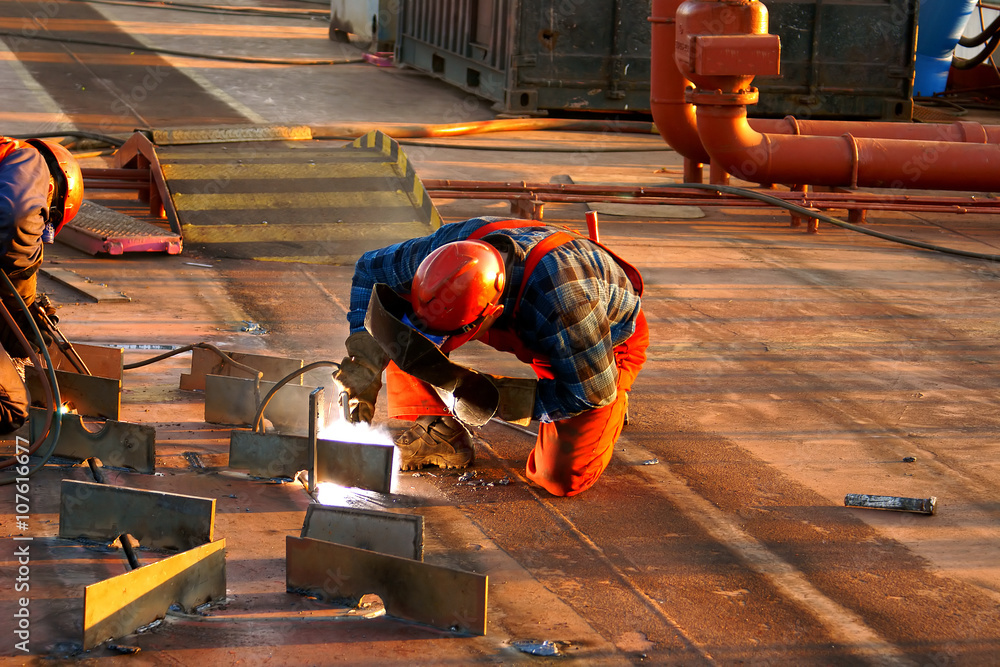Shipyard welder during welding on the deck of the ship during the renovation - obrazy, fototapety, plakaty 