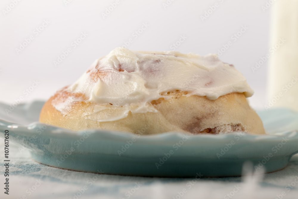 Freshly baked homemade cinnamon roll with cream cheese buttercream frosting and an antique bottle of milk macro shot
