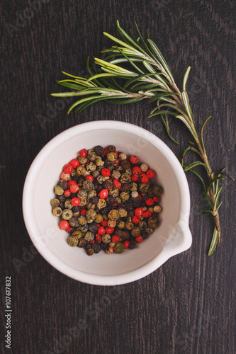 a mixture of peppers ( red, black , white ) in a white mortar with a sprig of rosemary